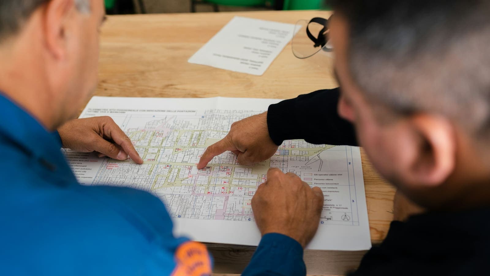 Deux personnes en tenue de travail pointent un plan imprimé posé sur une table.