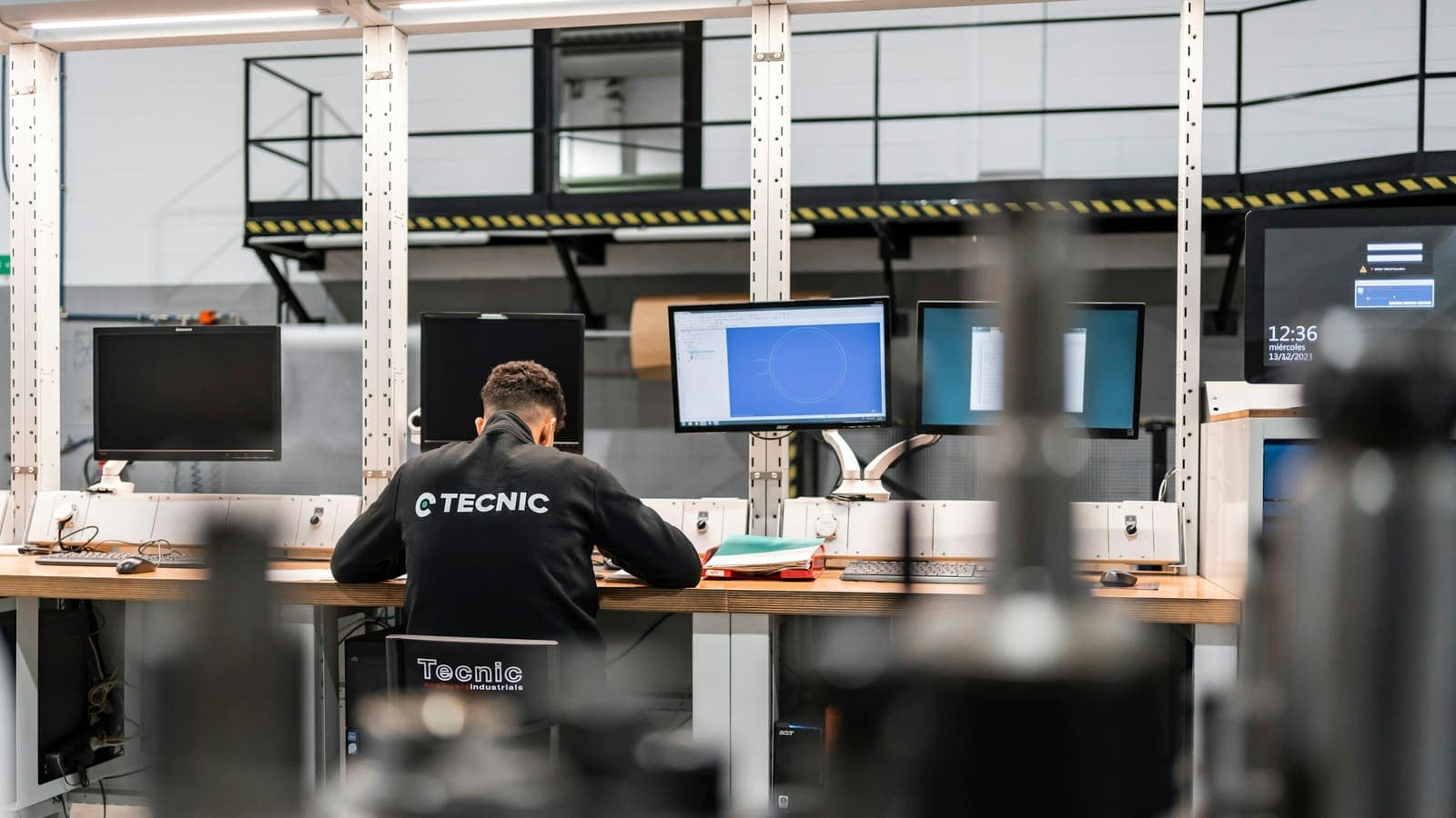 Un technicien devant plusieurs écrans d'ordinateur, au bord de l'atelier.