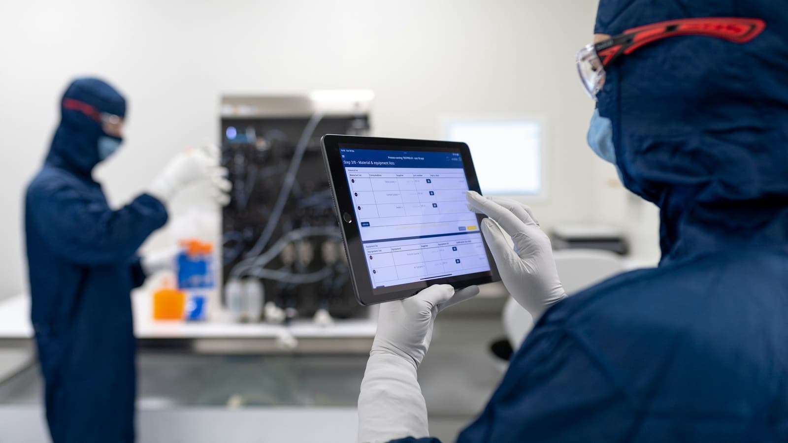 Des techniciens en tenue de protection consultent une tablette à côté d'un équipement.